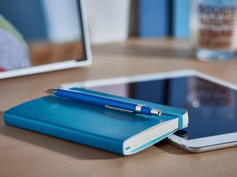 Ein Block, mit einem Stift liegen neben einem Tablet auf einem Tisch.