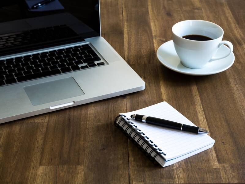 Ein Block, Stift, Notebook und eine Kaffeetasse stehen auf dem Tisch.